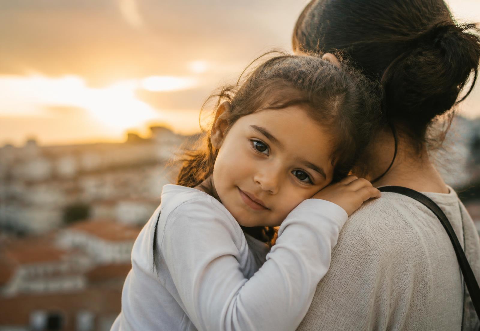 A child resting on a parent's shoulder in warm evening light